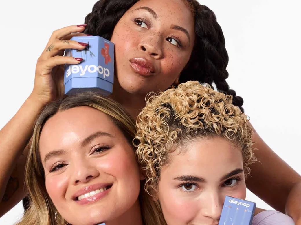 Three women smiling together, holding Alleyoop products to their faces.